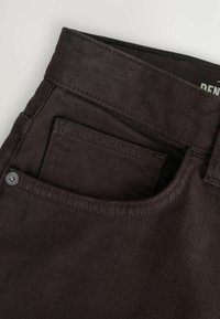 I jeans di denim marrone presentano una tasca frontale con cuciture visibili e un bottone in metallo. Il tessuto ha una finitura testurizzata e una leggera costina.