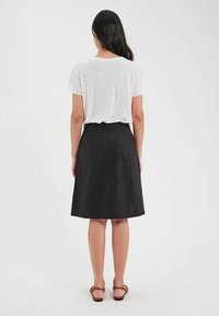 Jupe noire mi-longue avec une texture lisse, une taille définie et des détails de couture subtils. Associée à un t-shirt blanc uni et des sandales.