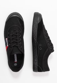 Black canvas sneakers with rubber toe cap and textured sole, featuring a red and blue accent tag, round laces, and perforated eyelets.