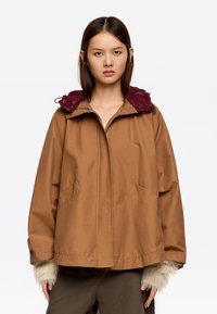 Brązowa kurtka z bordową, ocieplaną kapturem, dwiema przednimi kieszeniami oraz futrzanymi akcentami na mankietach; luźny krój.