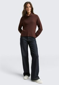 Bruine geribde coltrui in combinatie met donkerblauwe wijde jeans en witte sneakers. De outfit heeft een relaxte pasvorm en een casual ontwerp.