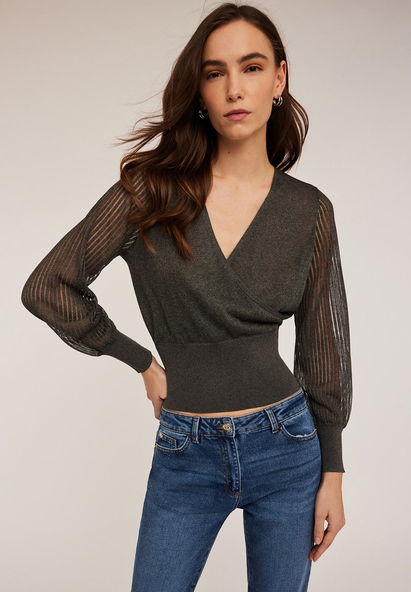 Top lung cu maneci lungi de culoare gri închis, cu decolteu în V și textură cu dungi. Mânecile sunt din material transparent în dungi, iar talia este ajustată. Este purtat cu blugi din denim albastru.