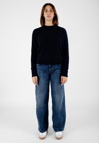 Maglione morbido blu navy con scollatura rotonda, abbinato a jeans in denim blu a vestibilità ampia e sneakers bianche con suola marrone chiaro.