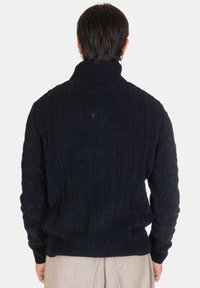 Maglione lavorato a maglia in un blu navy scuro. Caratterizzato da un alto colletto, texture a coste e maniche lunghe. Il design include motivi di maglia verticali e diagonali.