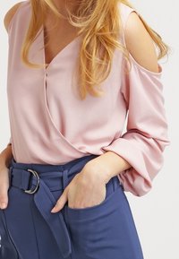 Blusa rosa chiaro con design a spalle scoperte, caratterizzata da uno stile avvolgente. Abbinata a pantaloni navy a vita alta e una cintura con una fibbia argentata.