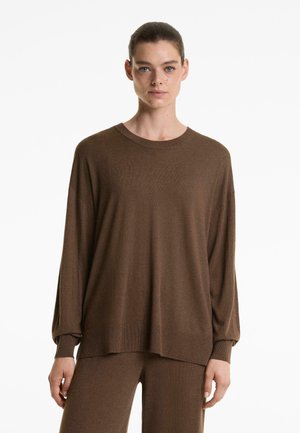 Pullover in maglia marrone, maniche lunghe, scollatura rotonda, vestibilità rilassata, polsini e orlo a coste, texture morbida. Indossato con pantaloni marroni coordinati.
