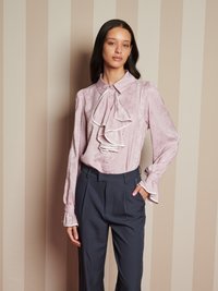 Blusa rosa chiaro con dettagli arricciati sul davanti, dotata di maniche lunghe e chiusura con bottoni. Abbinate a pantaloni grigi scuri a vita alta.