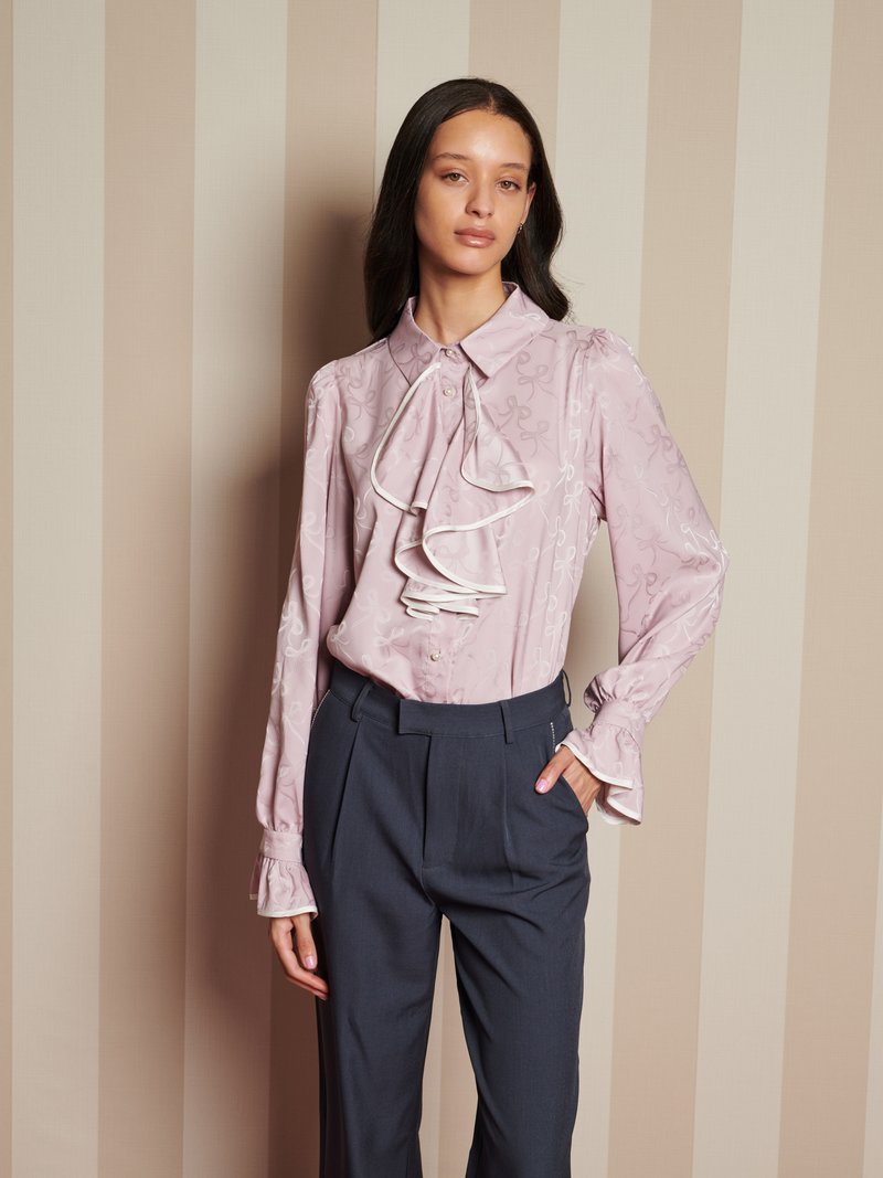 Blusa rosa chiaro con dettagli arricciati sul davanti, dotata di maniche lunghe e chiusura con bottoni. Abbinate a pantaloni grigi scuri a vita alta.