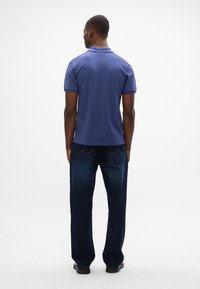 Polo shirt blu navy con maniche corte, tessuto testurizzato e colletto piatto, abbinato a jeans blu scuro con tasche posteriori e vestibilità a gamba dritta.