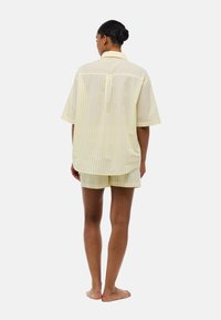 Chemise à manches courtes rayée jaune et blanche avec un empiècement au dos et un short assorti, fabriquée en tissu léger.