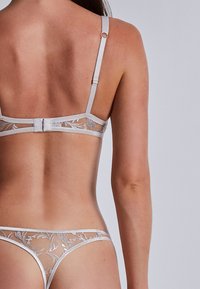 Ensemble de lingerie gris clair mettant en avant des panneaux en dentelle transparente avec broderie florale. Le soutien-gorge possède des bretelles ajustables et une fermeture à crochet au dos.