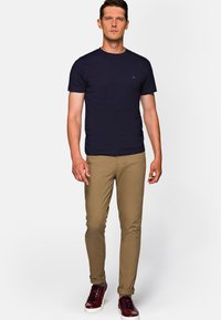 Granatowa bawełniana koszulka zestawiona z khaki wąskimi spodniami chinos i burgundowymi trampkami z białymi podeszwami. Koszulka ma małe niebieskie logo.