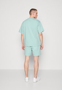 Set de tricou și pantaloni scurți din bumbac de culoare verde mentă. Tricoul are o croială relaxată, mâneci scurte și un design simplu. Pantalonii scurți sunt, de asemenea, simpli, având un tiv elastic.