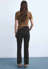Brown ribbed short-sleeve top paired with black flared jeans. The jeans feature a high waist and back pockets, and the model wears black strappy heels.