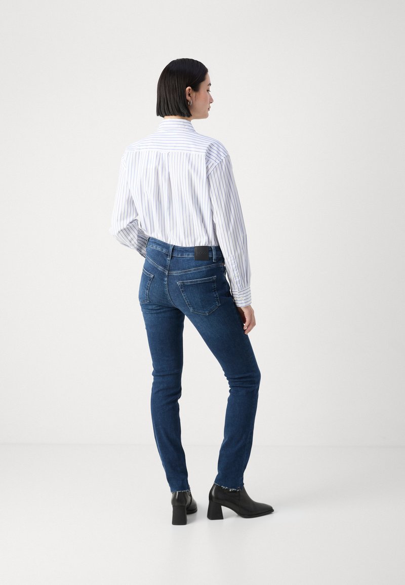 Camisa de botones a rayas blancas y azules combinada con pantalones ajustados de mezclilla azul oscuro. La camisa tiene un yugo trasero; los pantalones cuentan con bolsillos traseros. Botas negras de tacón.