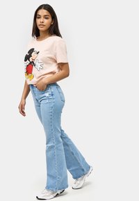 Jasnoróżowa koszulka z nadrukiem Myszki Mickey, zestawiona z jasnoniebieskimi dżinsami z szerokimi nogawkami, które mają przetarte wykończenie i subtelne detale w szwie.