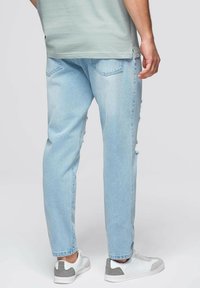 Vaqueros de denim azul claro con detalles desgastados, corte recto, bolsillos laterales y traseros, combinados con zapatillas blancas y grises.