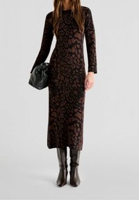 Braun gepunktetes Strickkleid mit figurbetontem Schnitt, langen Ärmeln, kombiniert mit einer schwarzen Clutch und knielangen braunen Stiefeln.