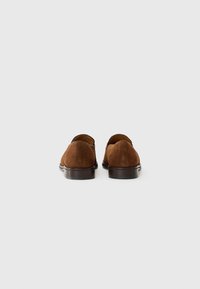 Mocassins en daim marron avec un bout arrondi, une bordure en cuir lisse autour de l'ouverture et un talon empilé bas. Texture subtile et design épuré.