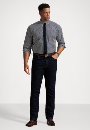 Chemise à rayures avec manches retroussées, jean en denim sombre, chaussures en cuir marron et ceinture assortie. Les accessoires incluent une montre.