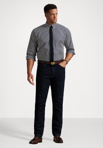 Camisa de molho com riscas azul-marinho e brancas, combinada com jeans escuros, gravata azul-marinho lisa, cinto de couro castanho e sapatos castanhos.