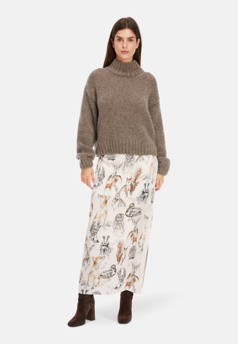 Brauner, gestrickter Rollkragenpullover kombiniert mit einem weißen Rock, der bunte Tierillustrationen zeigt; Model trägt braune Wildleder-Stiefeletten.