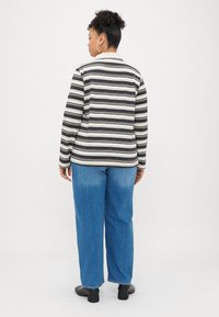 Svītraina garām piedurknēm krekls melnā un krēmkrāsā ar apkakles dekoltē, apvienots ar ziliem plašiem džinsiem un melnām kurpēm. Aizmugures skats.