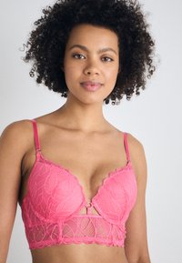 Pink lace bra with a floral leaf pattern, featuring adjustable straps and a lower lace band. Includes a front closure detail.