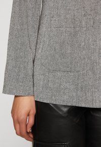 Haut gris texturé avec ourlet arrondi et manches aux coudes, associé à un pantalon en cuir noir avec un détail de poche latérale.