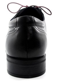 Zapato de cuero negro con punta redondeada y textura suave. Presenta un tacón bajo, detalles de costura sutiles y cordones burdeos.