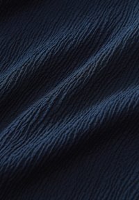 Tessuto blu navy con una superficie testurizzata e increspata che crea onde e pieghe, evidenziando la sua qualità tattile unica e la profondità.