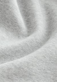 Tejido gris claro con una textura suave y lisa y un sutil patrón jaspeado. El material parece elástico y ligero, adecuado para el uso casual.