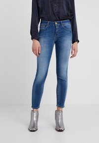 Jean skinny bleu clair en denim, avec une taille mi-haute, un léger délavage et des poches avant. Associé à des bottines argentées.