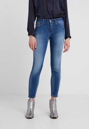 Jean skinny bleu clair en denim, avec une taille mi-haute, un léger délavage et des poches avant. Associé à des bottines argentées.