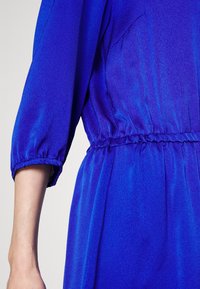 Vestido azul con una tela texturizada, mangas hasta el codo y una cintura elástica. La prenda tiene un diseño suave y fluido.