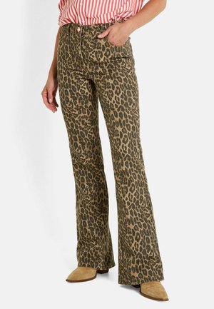 Pantalones acampanados con estampado de leopardo en oliva y marrón oscuro, con bolsillos frontales y costuras sutiles, combinados con botas de tobillo color beige.