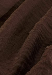 Tissu en velours côtelé marron foncé doux avec des rainures verticales visibles et des plis créant une surface texturée et ondulée.