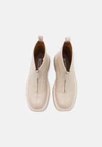 Botines de cuero beige hasta el tobillo con cierre de cremallera, suela acanalada y una lengüeta en la parte posterior. Textura suave y detalles de costura mínimos.