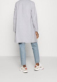 Lys grå lang frakke med lange ærmer, parret med lyseblå jeans og hvide sneakers med dyreprint-detaljer og broderede detaljer.