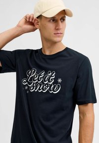 Zwarte T-shirt met korte mouwen, voorzien van de tekst "Laat het sneeuwen" in witte cursieve letters met sneeuwvlokaccenten. Gemaakt van zacht katoen, met een ronde hals.