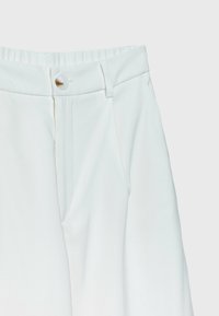 Pantalon blanc taille haute avec fermeture par bouton, braguette zippée, passants de ceinture et poches latérales sur fond uni clair.