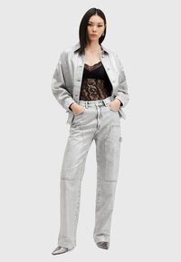 Chaqueta de mezclilla gris y pantalones a juego de corte holgado, combinados con una blusa de encaje negra. Tacones plateados con punta completan el conjunto.