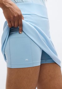 Αθλητικό σορτς ανοιχτού γαλάζιου χρώματος από ελαστικό ύφασμα, με εφαρμοστή γραμμή, ραφές και μικρό λογότυπο στην αριστερή πλευρά.