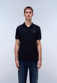 Polo blu navy in cotone, con colletto, patta con tre bottoni e piccolo logo sul petto. Abbinata a jeans in denim.