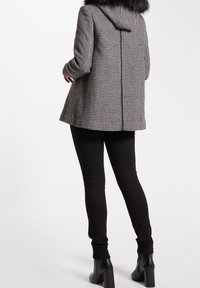 Cappotto in tessuto scozzese grigio e nero con cappuccio in pelliccia sintetica removibile. Abbinato a pantaloni neri aderenti e stivali con tacco alto.