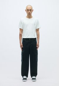 Λευκό κοντομάνικο μπλουζάκι συνδυασμένο με φαρδιά σκούρα cargo παντελόνια που διαθέτουν πολλές τσέπες και φερμουάρ. Μαύρα αθλητικά παπούτσια ολοκληρώνουν το σύνολο.