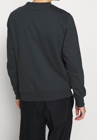 Ciemnoszara bluza z długimi rękawami, okrągłym dekoltem i prążkowanymi ściągaczami; wykonana z miękkiej bawełnianej mieszanki, z minimalistycznym wzorem i bez widocznych dekoracji.