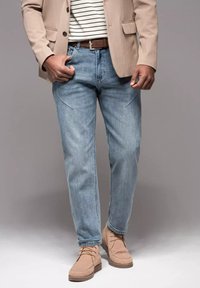 Jeans de denim azul claro con un corte relajado, que presentan bolsillos frontales y un sutil desgaste. Combinados con un blazer beige y zapatos beige.