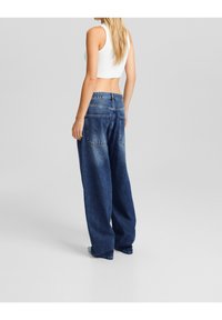 Rovné modré džíny z denimu s vybledlým vzhledem, se zadními kapsami a vysokým pasem. Stylizováno s bílým cropped topem.