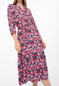 Vestido midi floral que presenta un vibrante patrón en rosa, azul y blanco, con escote en V, mangas tres cuartos y un lazo en la cintura.